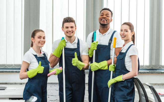 happy multicultural team of cleaners looking at camera and showing thumbs up